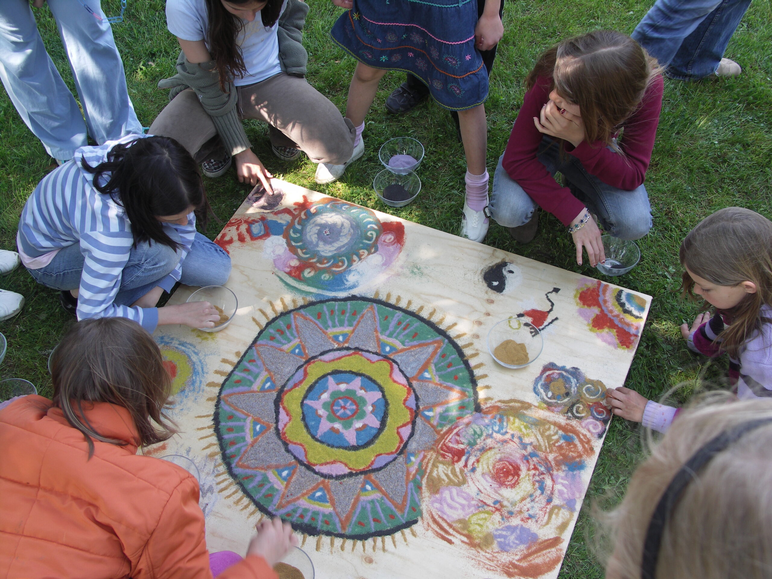 Children are painting a large mandala poster together in a meadow